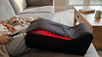 man holding controller using red light therapy for legs unit on the couch