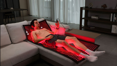 man laying on red light therapy mat while holding controller