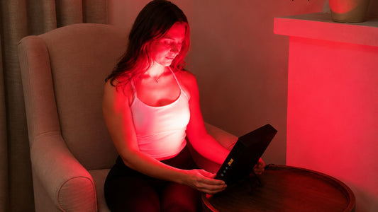 woman holding red light therapy panel while sitting in chair