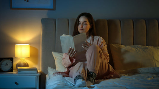 woman reading a book while laying in bed with a light next to her