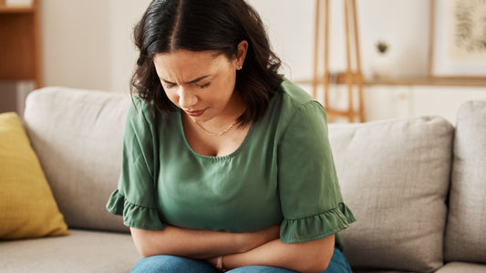 woman sitting on couch wearing a green top in discomfort in her stomach