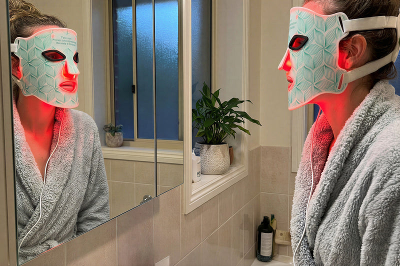 Woman Wearing LED Light Therapy Mask While Staring into reflection in mirror