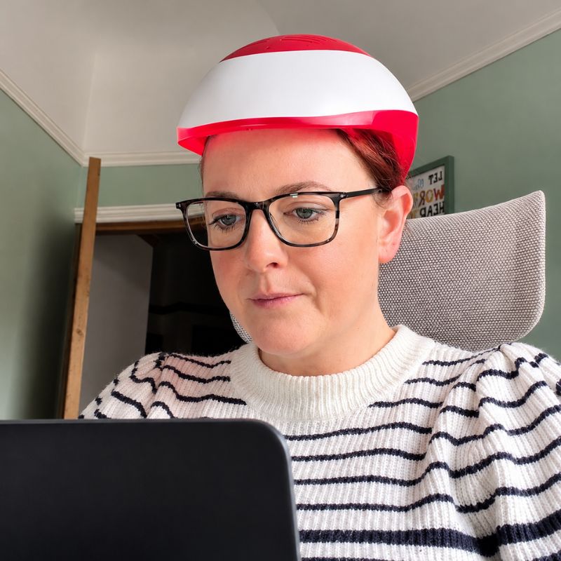 laserlighttherapyhelmetwomanworkingonlaptopwhilewearinghelmet
