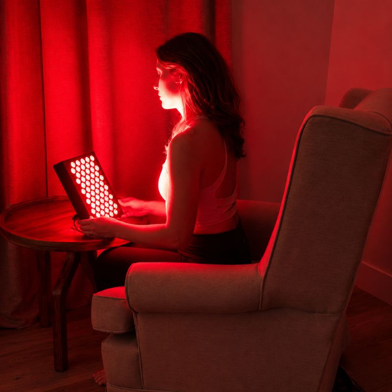 sr60redlighttherapypanelwithwomanholdingitwhilesittinginchair